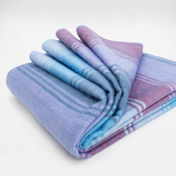 Tinizaray baby alpaca wool blanket – a soft, folded blanket with blue and purple stripes rests neatly on a plain surface, showcasing its vibrant colors and texture in a clean, bright environment