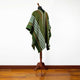 A green poncho with white and brown stripes is displayed on a wooden stand in a room with wooden flooring and a plain white wall background.