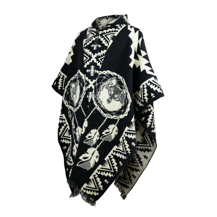 A black and white poncho features a geometric pattern with dreamcatcher designs and wolf imagery. It is draped on a display, highlighting its intricate motifs and fringed edges.