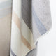 Yankuam baby alpaca wool blanket – a soft fabric features horizontal stripes in muted tones of gray, beige, and white, flowing gently in draped folds against a plain background