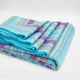 Tzacantza baby alpaca wool blanket – a folded, multicolored striped blanket lies on a plain white surface, displaying shades of blue, purple, and yellow in a tidy arrangement