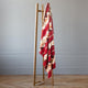 A red patterned blanket drapes over a wooden stand. It's positioned in a room with light gray walls and a parquet floor, creating a minimalist, cozy atmosphere.