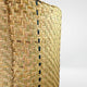 A close-up of a woven basket with an intricate herringbone pattern, displaying yellow and greenish hues, with a few dark vertical accents, set against a plain white background.