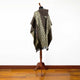 A patterned poncho with geometric designs hangs on a mannequin, displayed in a room with wooden flooring and a plain white wall.