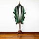 A green and white poncho with a hood is displayed on a wooden mannequin stand against a plain white wall, on a wooden floor.