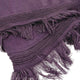 A purple fringed textile lies folded, featuring intricate embroidered patterns along the edges, creating a decorative and cozy appearance suitable for a stylish home setting.