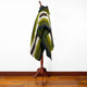A striped green and white poncho is displayed on a wooden mannequin stand. The setting includes a polished wooden floor and a plain white wall background.