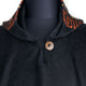 A black woolen garment with a decorative collar featuring red patterns is fastened with a round, textured button. The garment is displayed on a black mannequin torso against a plain background.