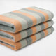 Tumbunuma baby alpaca wool blanket – three folded wool blankets, striped with orange, gray, and light green hues, are stacked neatly against a plain white background