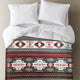 A bed features white pillows and a comforter with intricate geometric patterns in red, black, and beige. The setting is simple and neutral, highlighting the vibrant design.