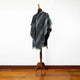 Nambija lightweight alpaca wool hooded poncho – a black and gray hooded poncho with diamond patterns is displayed on a wooden mannequin stand, situated against a white wall and resting on a wooden floor