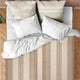 Zhumir baby alpaca wool blanket – a bed features crumpled white linens and four pillows, two with beige covers displaying text: HAPPINESS, RELAX, FREEDOM, WELLNESS, and TAKE A BREAK. The room has wooden herringbone flooring
