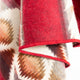 A folded wool blanket displays red, brown, and cream geometric patterns. The blanket is layered, highlighting its textured and warm appearance, set against a plain background.