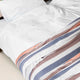 Sopoto baby alpaca wool blanket – a bed is covered with white sheets and striped bedding in blue, brown, and orange, set in a neatly arranged, well-lit bedroom