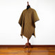 A colorful poncho with diagonal stripes is displayed on a mannequin. It stands on a wooden floor against a plain white wall.