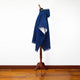 Mannequin displays a blue hooded poncho draped elegantly, featuring a subtle decorative trim. It stands on a wooden floor against a plain white background, highlighting the garment's color and texture.