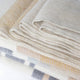 Yankuam baby alpaca wool blanket – stacked woolen blankets with soft textures and subtle pastel patterns lie neatly arranged, displaying varying shades of beige, blue, yellow, and gray, on a smooth surface