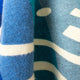 A close-up of a textured, multicolored fabric showing blue shades with white geometric patterns. The material appears soft, suggesting a cozy, woven textile, possibly part of a garment or accessory.