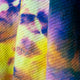 Colorful fabric displays a vibrant, tie-dye pattern, with shades of yellow, blue, purple, and pink, on a herringbone weave texture, creating a visually dynamic and textured surface.