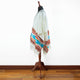 A shawl with colorful geometric patterns displayed on a wooden mannequin stand. The context is a wooden floor and white wall, providing a simple background.