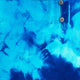 Blue tie-dye fabric with a waffle texture and abstract dark blue patterns, featuring a placket with two silver buttons, creating a casual, artistic appearance.