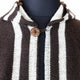 A striped woolen garment fastened by a single round button is displayed on a black mannequin, set against a plain background.