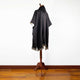 A dark gray poncho with fringe edges is displayed on a wooden mannequin stand, set against a plain white background and wooden floor.