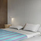 Tzacantza baby alpaca wool blanket – a neatly made bed with striped blue and purple bedding rests against a textured wall. Soft lighting highlights a small side table, creating a cozy, modern bedroom atmosphere