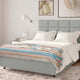 Nongora baby alpaca wool blanket – a neatly made bed, covered with a colorful striped blanket, stands in a serene bedroom. A wall-mounted lamp and framed art enhance the calm, cozy environment