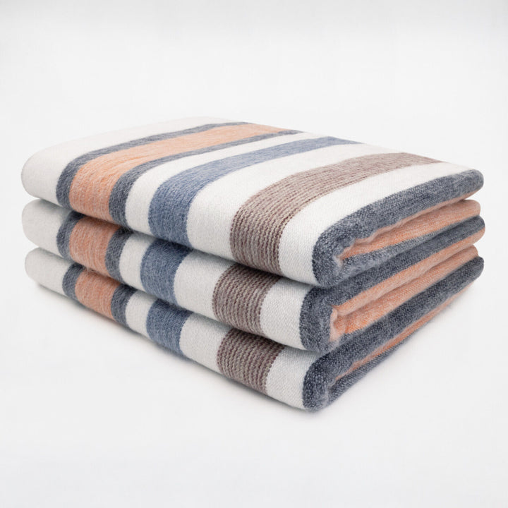 Sopoto baby alpaca wool blanket – a neatly folded stack of three striped blankets lies on a smooth white surface, featuring alternating bands of blue, white, peach, and brown colors