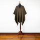 A brown checkered poncho displayed on a wooden mannequin stand, positioned against a plain white wall and resting on a wooden floor.