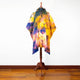 A colorful, tie-dyed poncho with a hood displayed on a wooden mannequin stand, set against a white wall and wooden floor background.