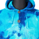 A tie-dye blue hoodie showcases two silver buttons on a textured knit fabric, displayed on a black mannequin torso, highlighting the garment's vibrant color and casual style.