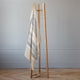 Yankuam baby alpaca wool blanket – a wooden clothes rack holds a beige and gray striped blanket, standing on a wooden floor against a pale gray wall in a minimalist room