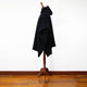 Achema llama wool hooded poncho – a black cloak drapes over a wooden mannequin stand, positioned on a polished wooden floor against a plain white wall
