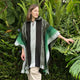 A person wearing a green and black hooded poncho gently touches lush, tropical foliage in a garden setting.