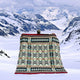 A person stands holding a large, intricately patterned blanket against a snowy mountainous landscape, surrounded by snow-covered peaks and a cloudy sky.