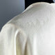 A cream-colored textured fabric is draped over a shoulder, with subtle patterns visible. The backdrop is solid gray, providing a neutral contrast.