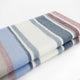 Pindo baby alpaca wool blanket – a folded, striped blanket lies on a flat surface. The blanket features alternating horizontal stripes in shades of blue, white, beige, and maroon against a plain, white background