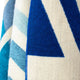 A woven fabric displays geometric patterns with large blue triangles and chevron stripes in shades of white and blue, creating a striking visual contrast in the textured surface.