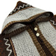 A knitted poncho with a hood displays a zigzag pattern in shades of brown, white, and black. It features two white buttons down the front, highlighting the texture.