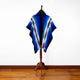 Wuachapa llama wool hooded poncho – a multicolored poncho with blue, white, and brown stripes drapes over a wooden mannequin in a minimalist room with a white wall and wooden floor