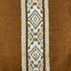 A brown knit fabric features a vertical intricate white geometric pattern, including diamonds and zigzags, running centrally. The surrounding area is a textured plain brown knit.
