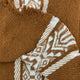 A woven brown and white fabric features intricate geometric patterns. It is folded, with visible fringed edges, suggesting warmth and craftsmanship in a cozy setting.