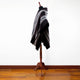 A mannequin displays a black and gray striped poncho against a plain white wall, standing on a polished wooden floor.