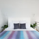 Tinizaray baby alpaca wool blanket – a neatly made bed with striped purple, blue, and grey bedding, flanked by potted plants, and set against a white paneled wall with two small, unobtrusive wall lights