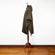 Zampu thick llama wool hooded poncho – a brown woven cloak with a hood is displayed on a wooden mannequin stand, set against a white wall and wooden floor in a minimalist setting