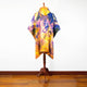 A colorful, tie-dye poncho hangs on a wooden stand, positioned against a white wall and hardwood floor.