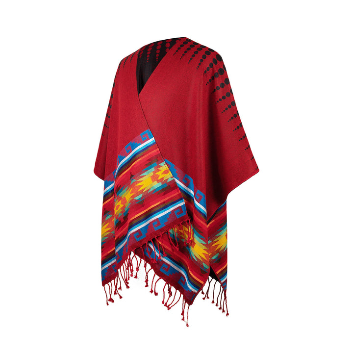 A red poncho with black dotted patterns features vibrant geometric designs in yellow, blue, and red along the edges, with tassels hanging from the hem in a simple background.