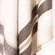 Quisapincha baby alpaca wool blanket – a draped, textured woolen fabric with beige, gray, and orange stripes, hanging softly, creating gentle folds, against a neutral backdrop